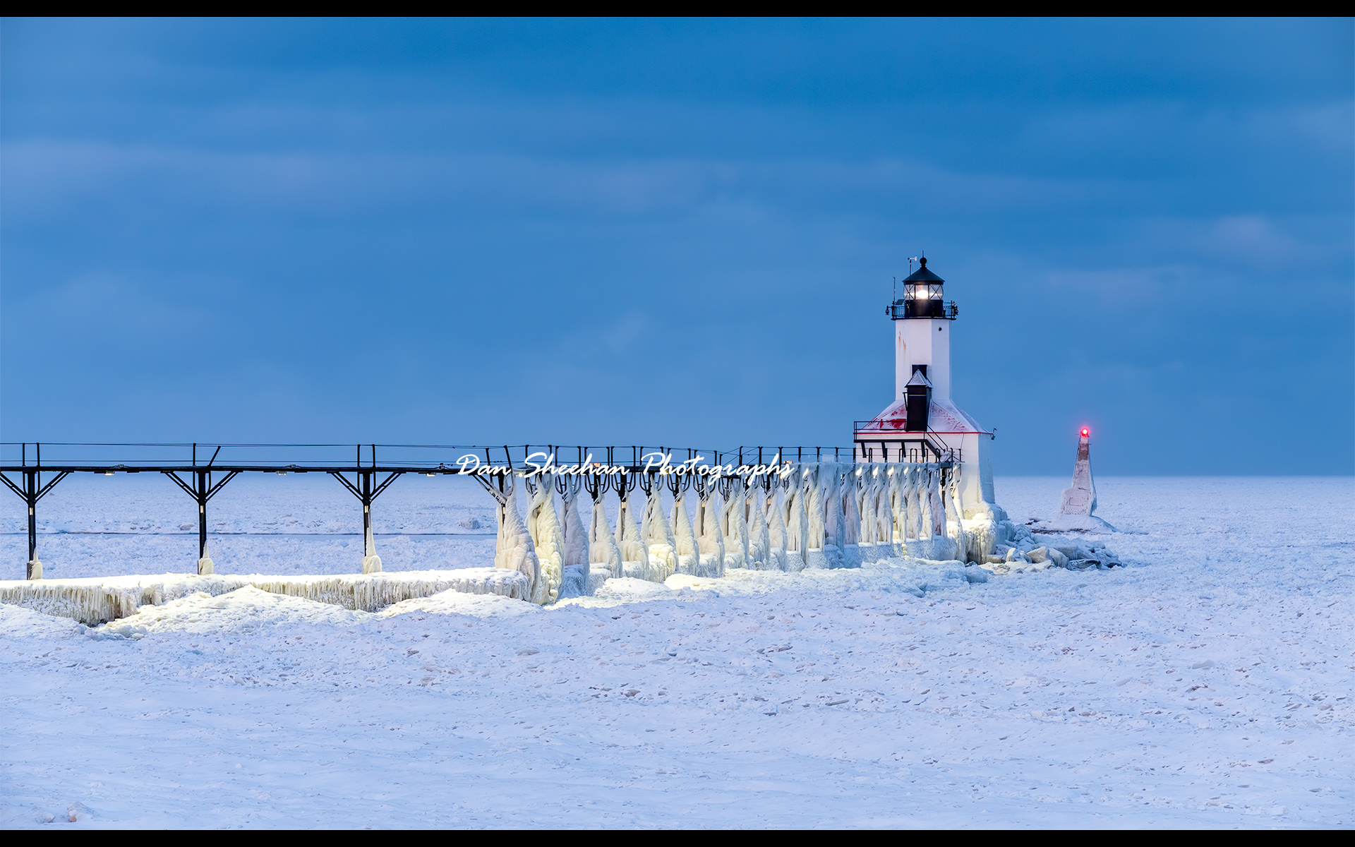 Bitter cold. The Michigan City, Indiana lighthouse photographed before dawn during the Polar Vortex. The temperature was well below zero not counting the famous wind chill factor which may have dropped the temp to a record or near record low. Lake Michigan frozen to the horizon and beyond. Two shades of blue in this photograph. The sky and the snow and ice covering the frozen lake which at this time of day records as more blue than white. Thank you, Mother Nature.  : Lighthouses : Dan Sheehan Photographs - Fine Art Stock Photography